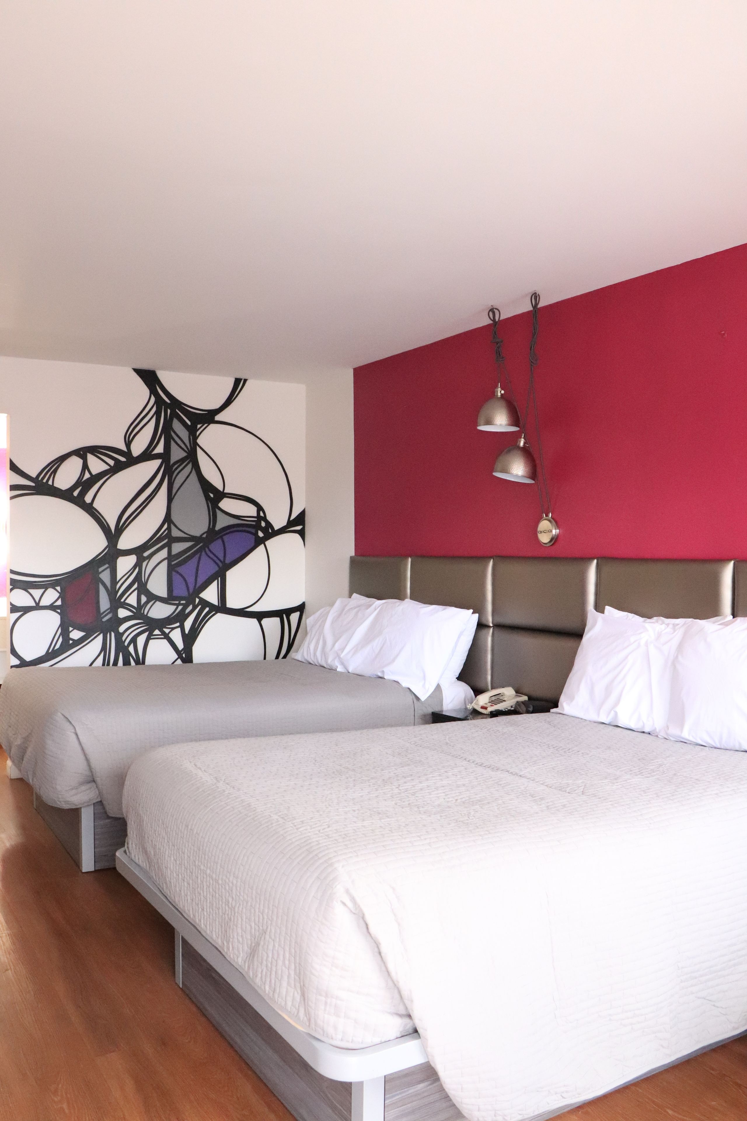 A hotel room with a large bed, a red accent wall, and a modern abstract art piece.