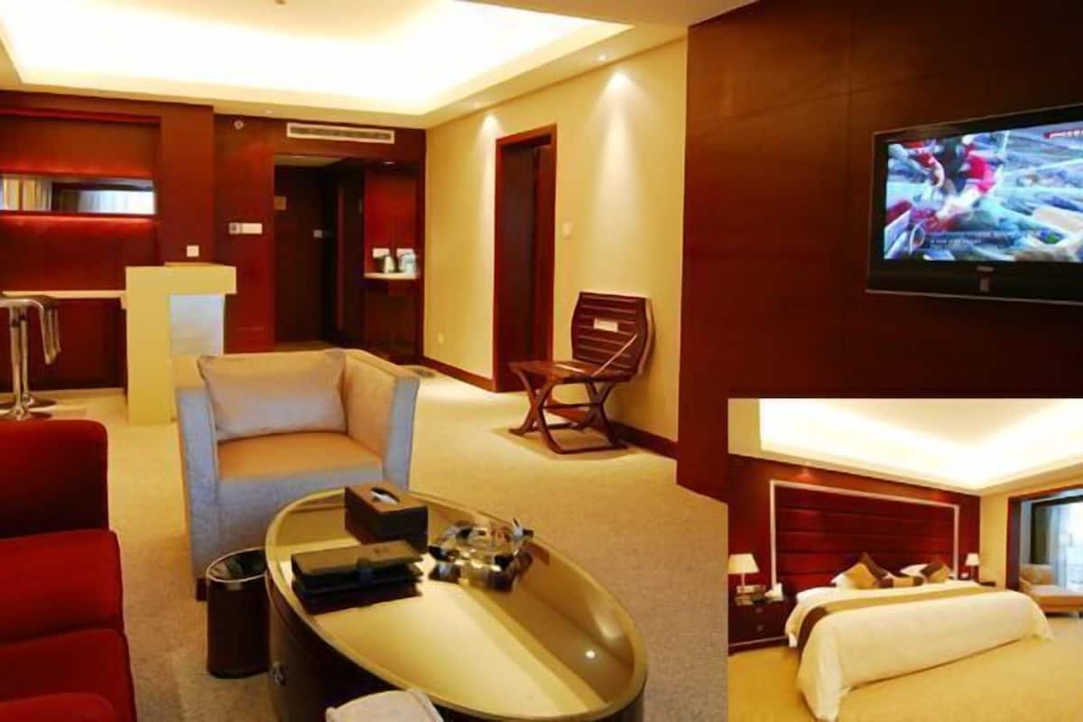 A hotel room with a red sofa, a small round table, a TV, and a bed with a white headboard.