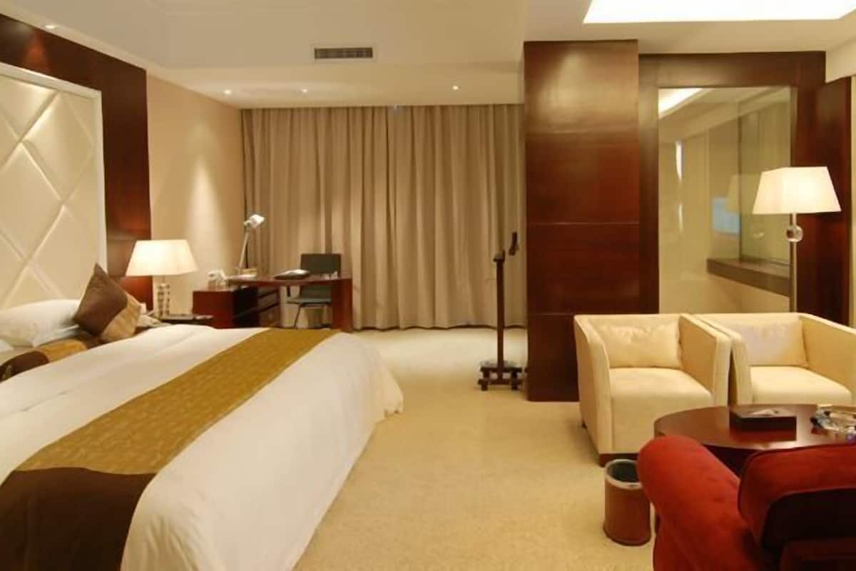 A hotel room with a large bed, a desk, a TV, and a red armchair.