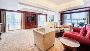 Ein Hotelzimmer mit großem Fenster, Fernseher, Sofa, Sessel und Couchtisch.