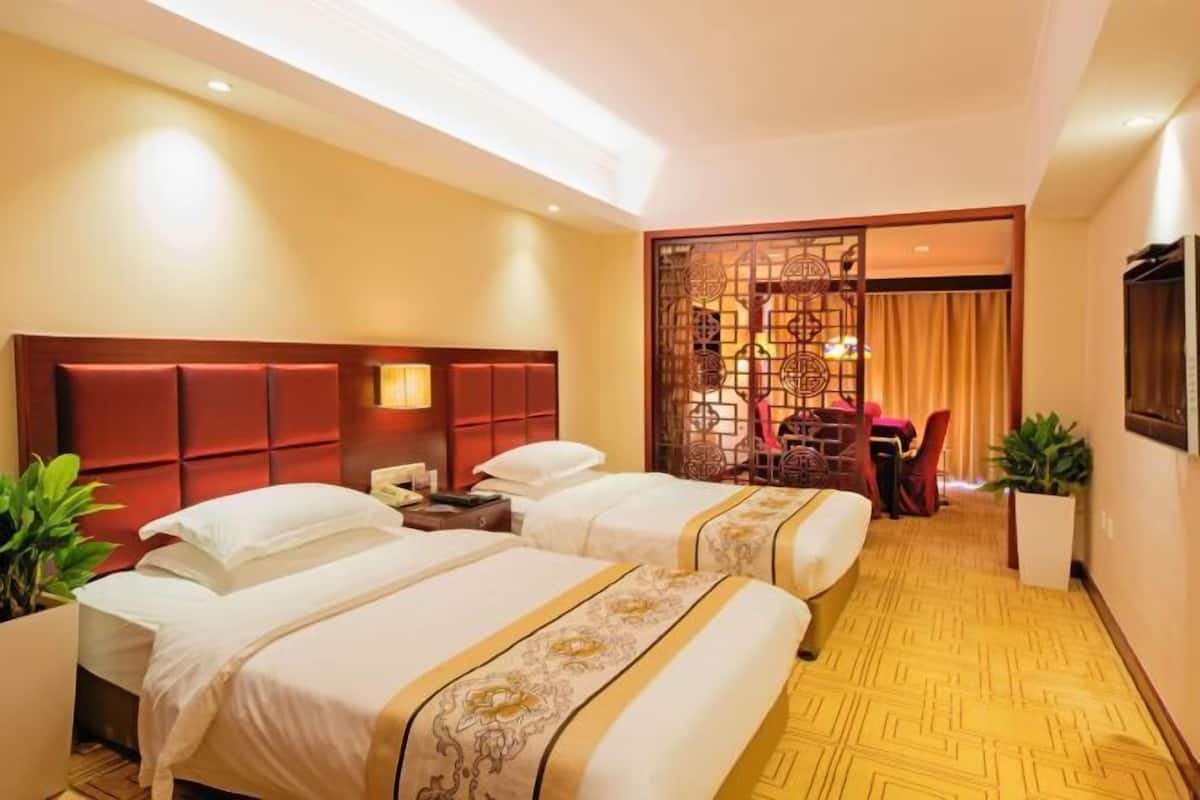 A hotel room with two beds, a wooden headboard, a desk with a chair, and a decorative screen.