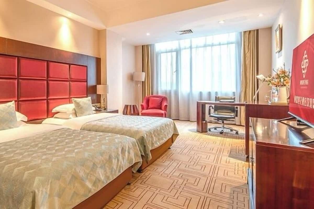 A hotel room with two beds, a desk, a chair, and a large window with curtains.