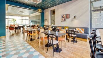 Un restaurante moderno con suelo de patrón hexagonal, varias zonas de estar que incluyen mesas y un sofá, y un techo con diseño geométrico.