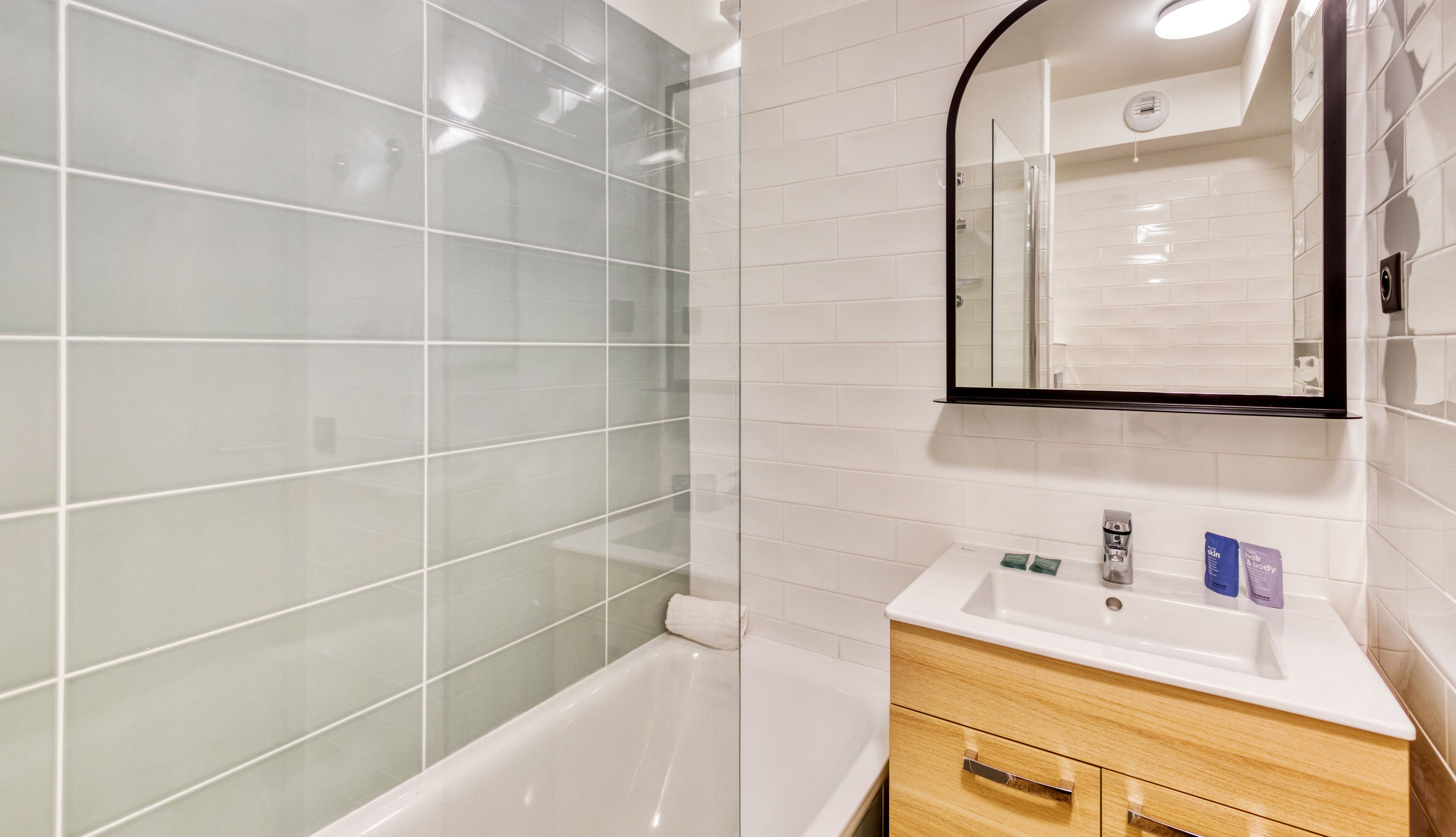 A modern bathroom with a glass shower enclosure, a white sink with toiletries, and a wooden vanity.