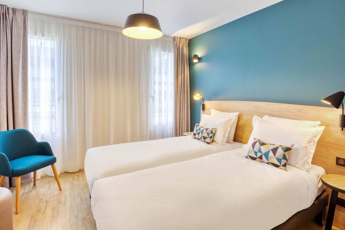 Una habitación de hotel con dos camas, un escritorio, una silla y una lámpara.