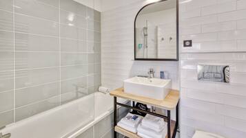 A modern bathroom with a white bathtub, a sink with a mirror above it, and a shelf with towels.
