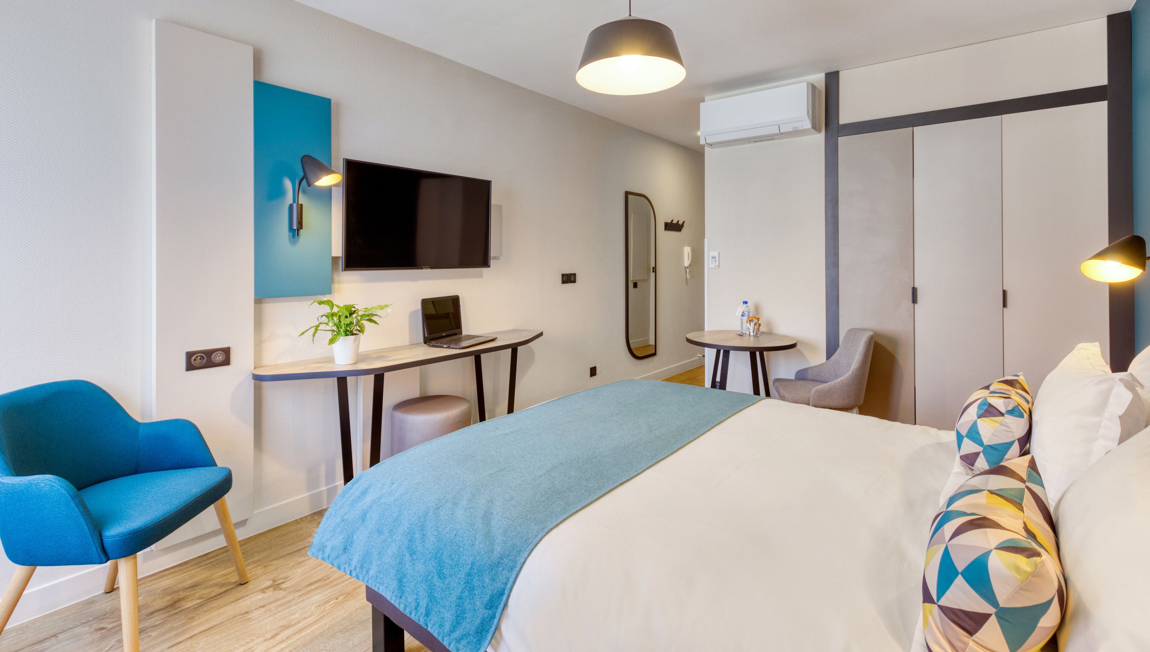 Een moderne hotelkamer met een bed, een bureau, een stoel, een televisie en een spiegel.