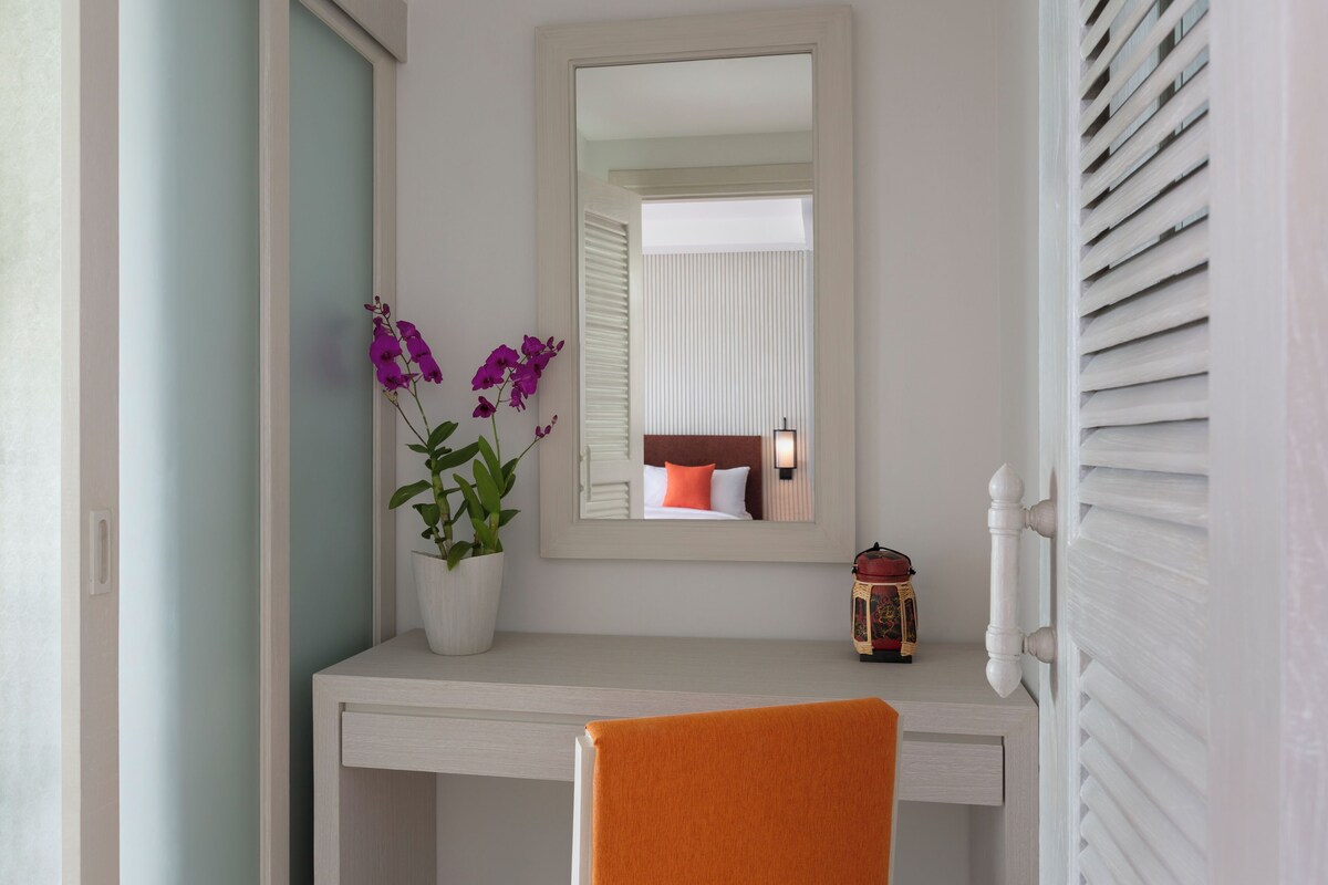 Een badkamer met een wit wastafelmeubel, een spiegel, een plant in een pot en een handdoekhouder.