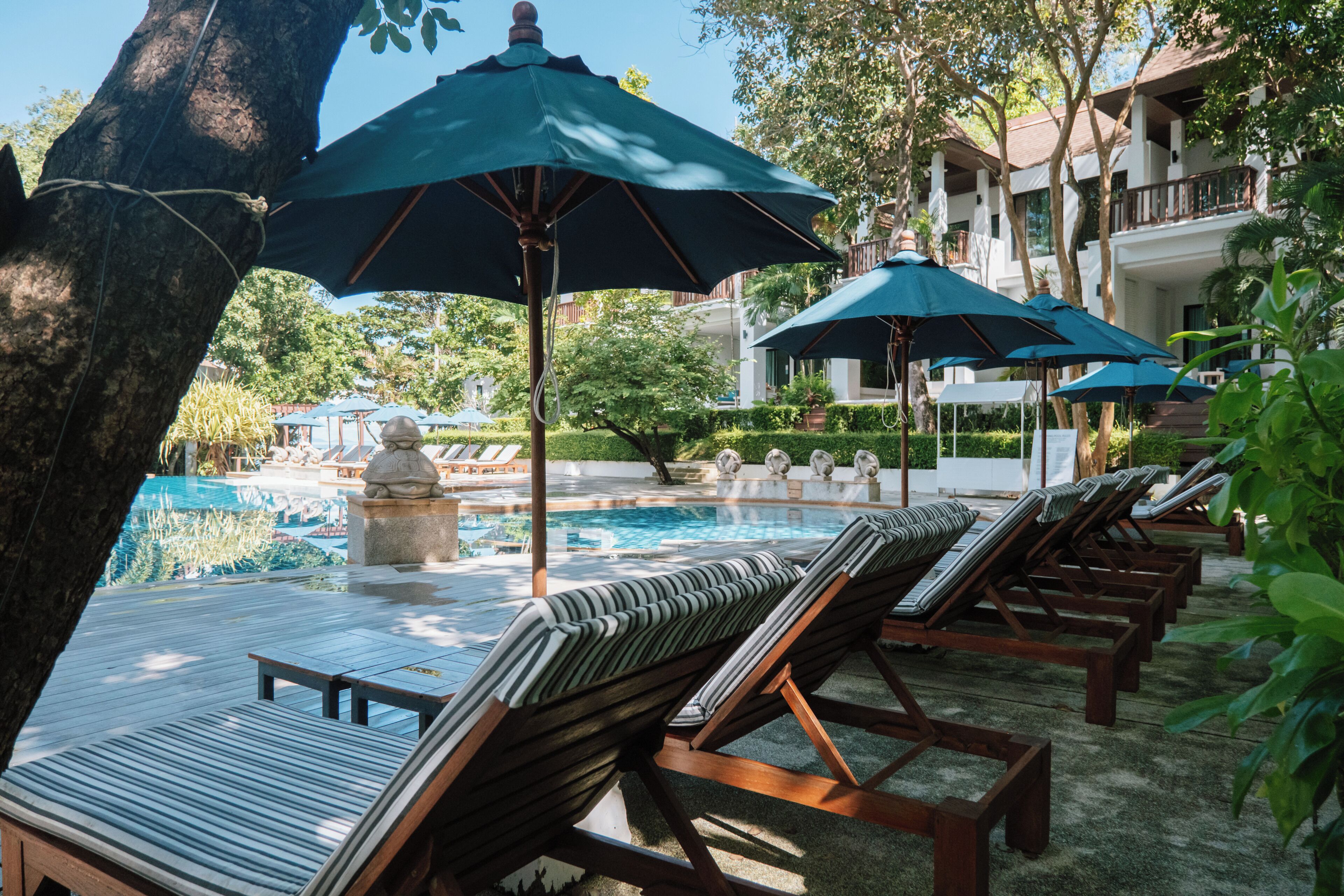 A poolside area with lounge chairs and umbrellas, a pool, and a building in the background.