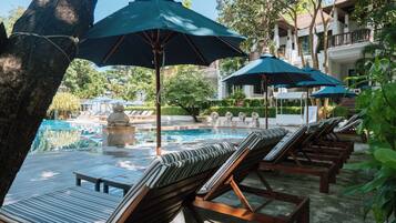 A poolside area with lounge chairs and umbrellas, a pool, and a building in the background.