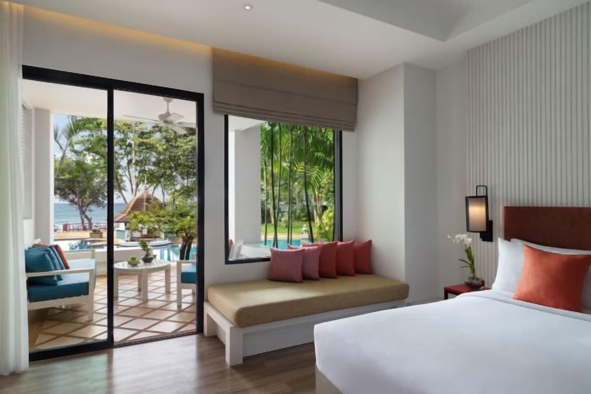 Habitación de hotel con una cama grande, zona de estar con vista a la piscina y balcón con vista al océano.