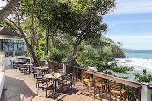 A deck with tables and chairs overlooking a coastal view.