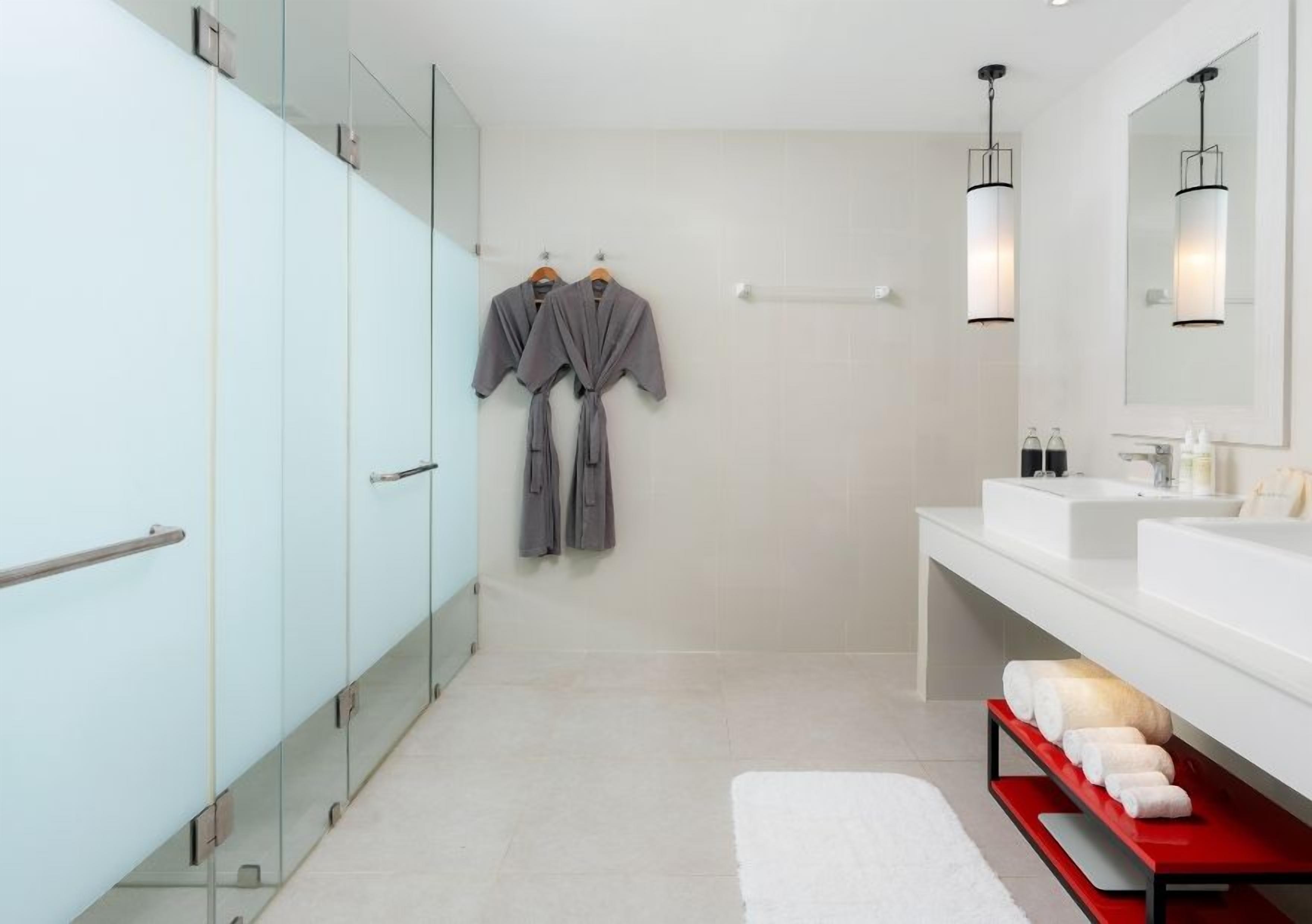 A modern bathroom with a glass shower enclosure, a white sink, and a red towel rack.