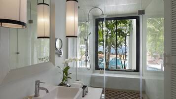 Une salle de bain moderne avec un grand miroir, deux lavabos, une douche et une fenêtre donnant sur une piscine et des palmiers.