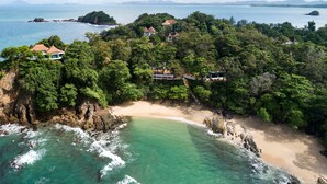 Vista aérea de una isla tropical con playa, costa rocosa y varios edificios rodeados de vegetación densa.
