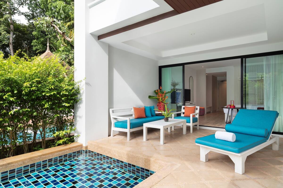 Un área de descanso al aire libre moderna con piscina, mobiliario blanco y vistas a la piscina y la vegetación.