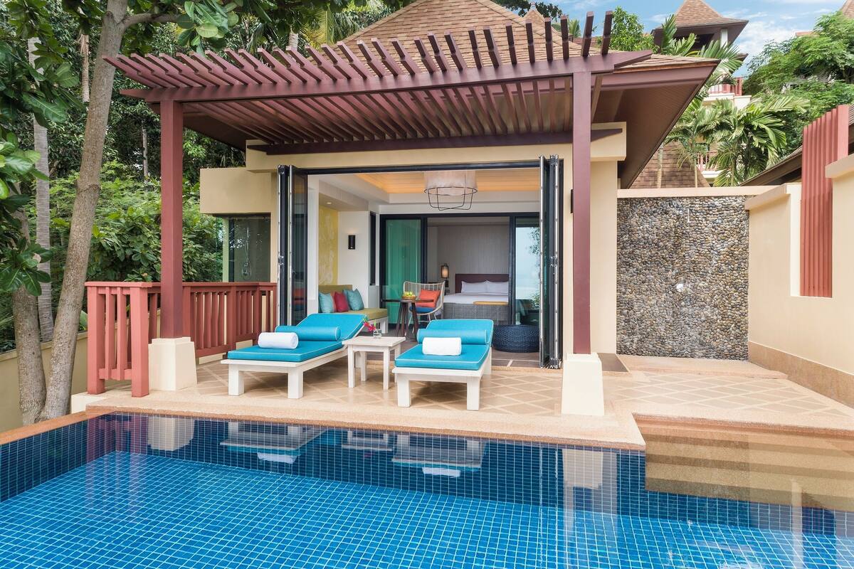 Un área junto a la piscina con sillones de descanso y una zona de estar cubierta.