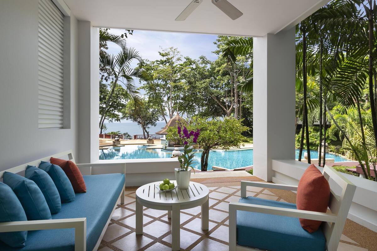 Un área de descanso moderna con vista a la piscina, que incluye un sofá, sillas y una mesita con una planta.