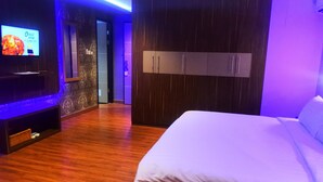 Habitación de hotel con cama, suelo de madera, televisor en la pared izquierda y armario de dos puertas.