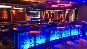 Zona de bar con mostrador iluminado con neón y varios taburetes.