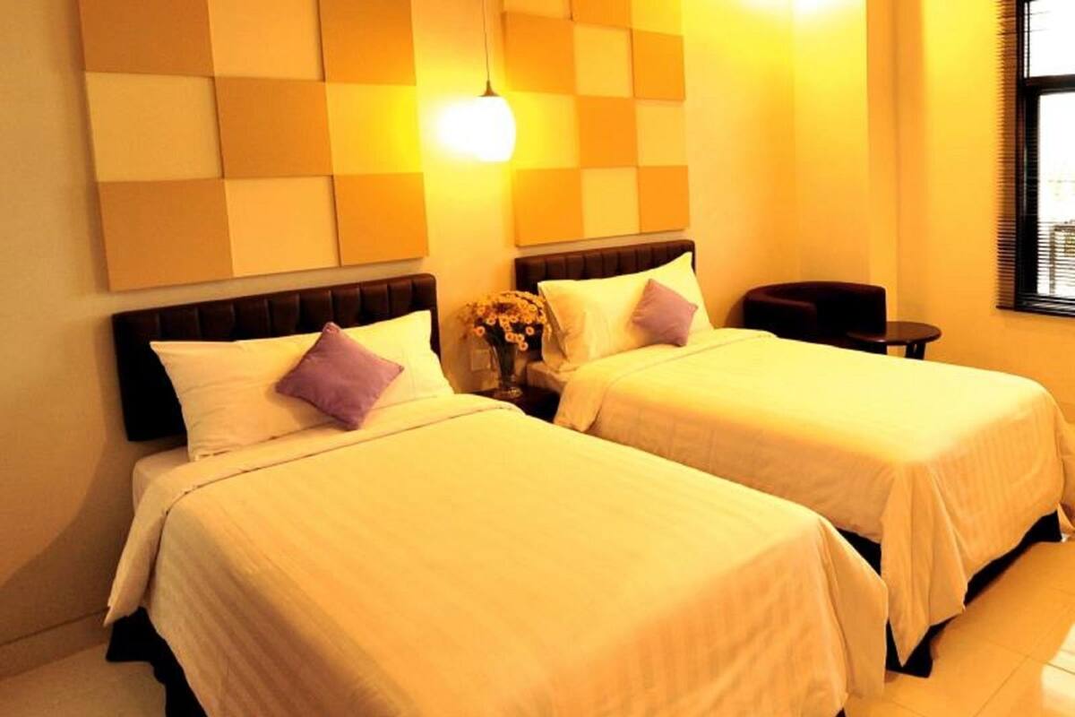 A hotel room with two beds, a nightstand, a small table, and a wall-mounted light fixture.