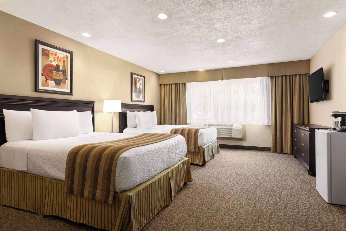 A hotel room with two beds, a television, a desk, and a window with curtains.