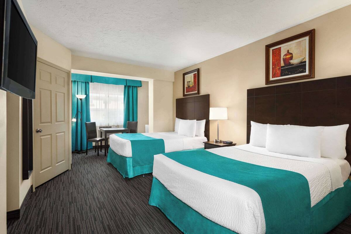 A hotel room with two beds, a desk, a chair, a TV, and a painting on the wall.