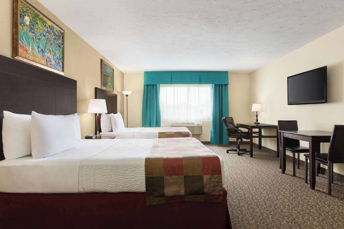 A hotel room with two beds, a desk, a chair, a TV, and a painting on the wall.