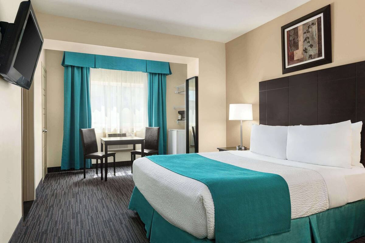 A hotel room with a bed, a desk, a chair, a television, and a painting on the wall.