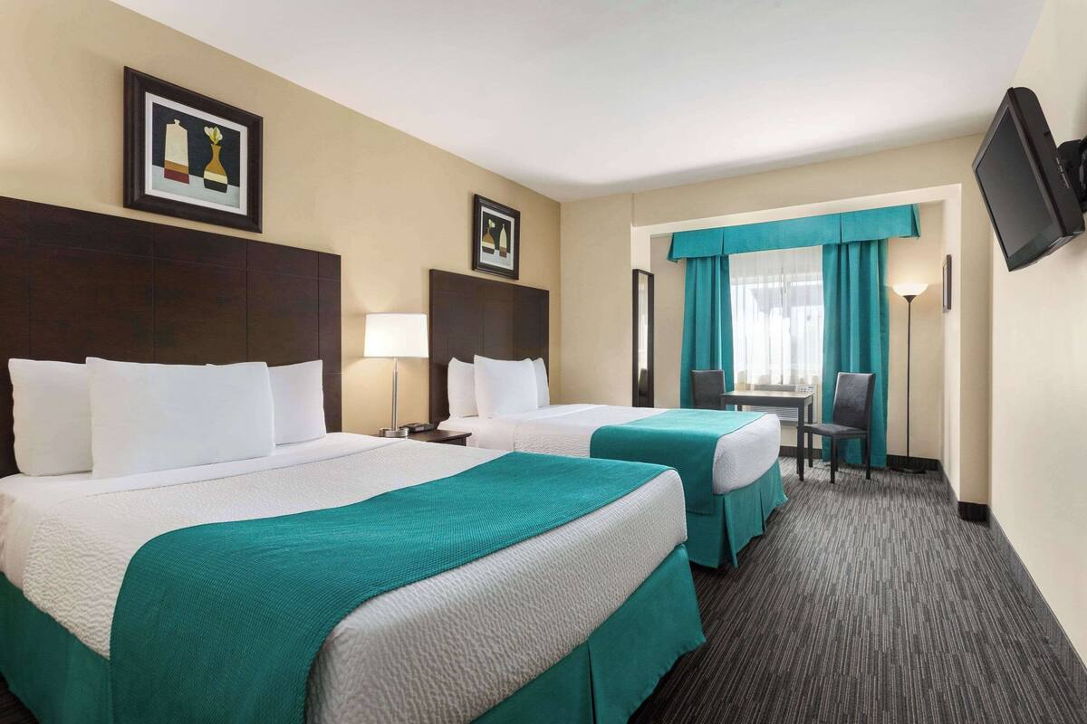 A hotel room with two beds, a desk, a chair, a TV, and artwork on the walls.