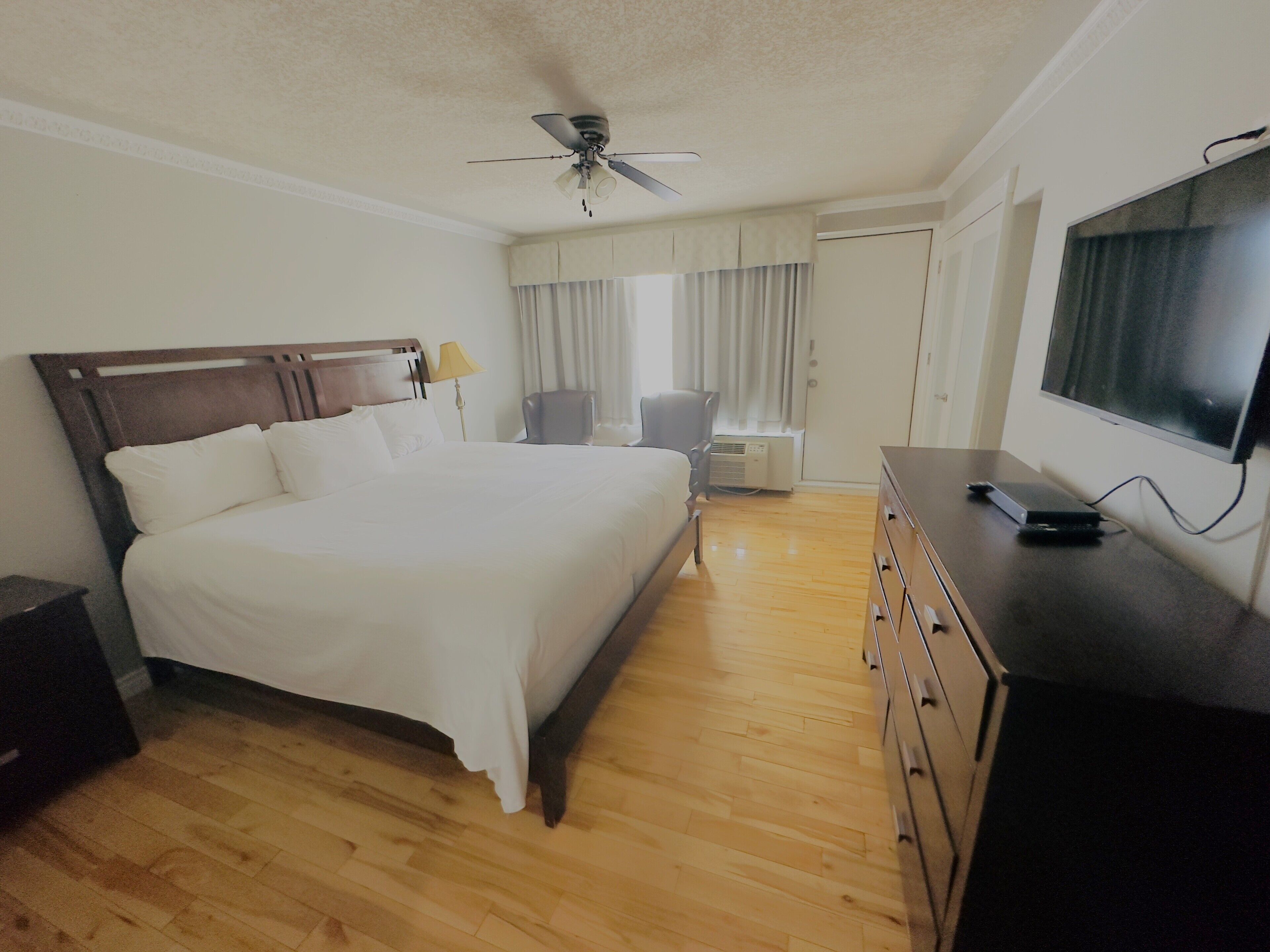 Una habitación de hotel con cama, escritorio con televisor, silla, ventilador de techo y armario.