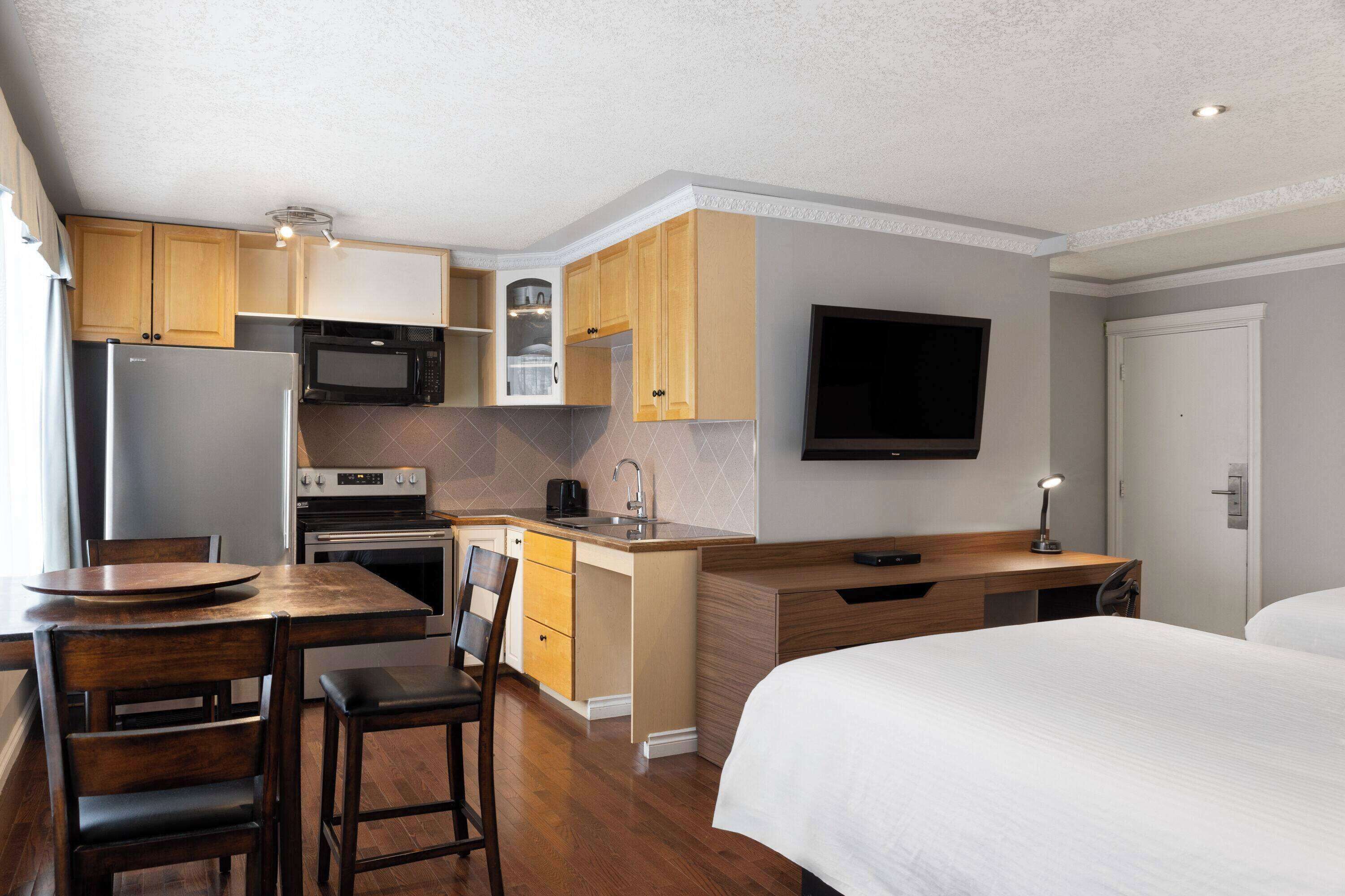 Une chambre d’hôtel de taille réduite, équipée d’une kitchenette, d’un lit, d’un bureau et d’une télévision.
