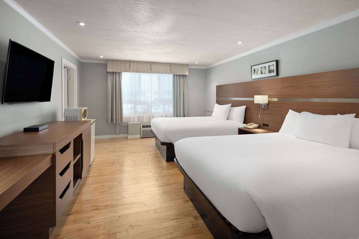 A hotel room with two beds, a desk, a television, and a window with curtains.