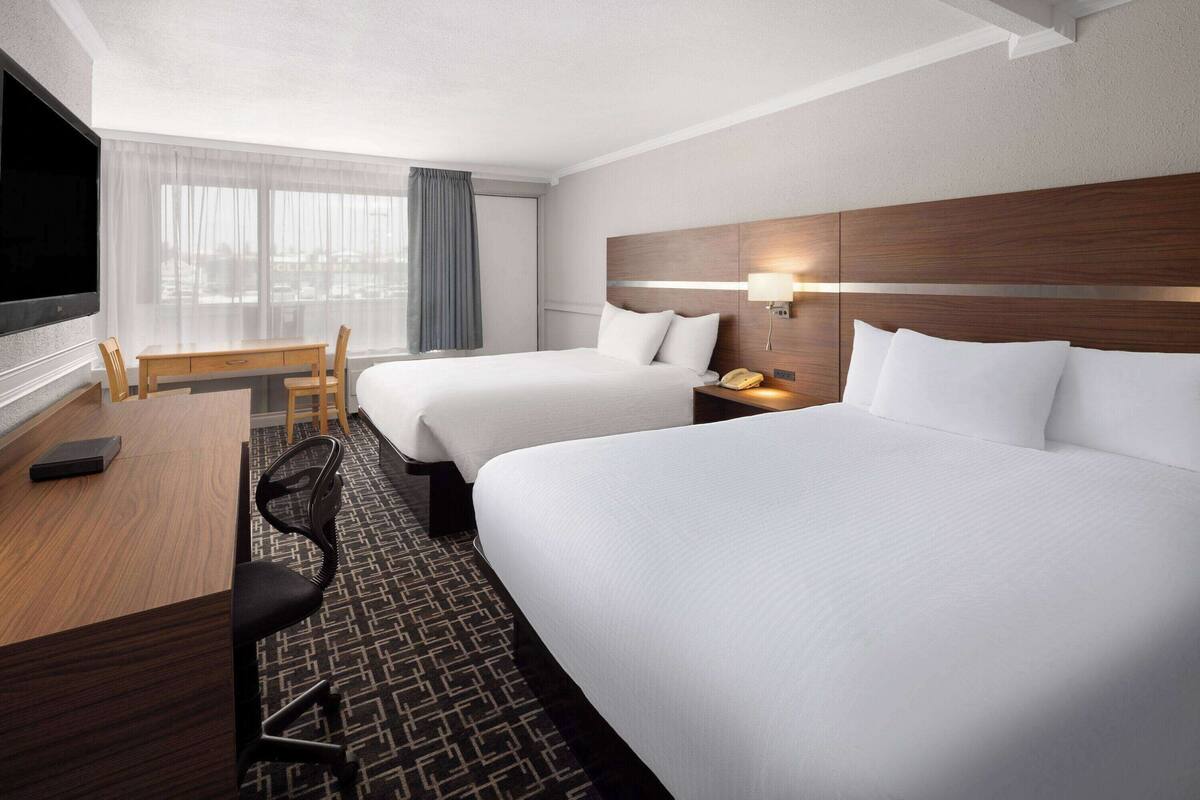 A hotel room with two beds, a desk, a chair, a TV, and a phone.