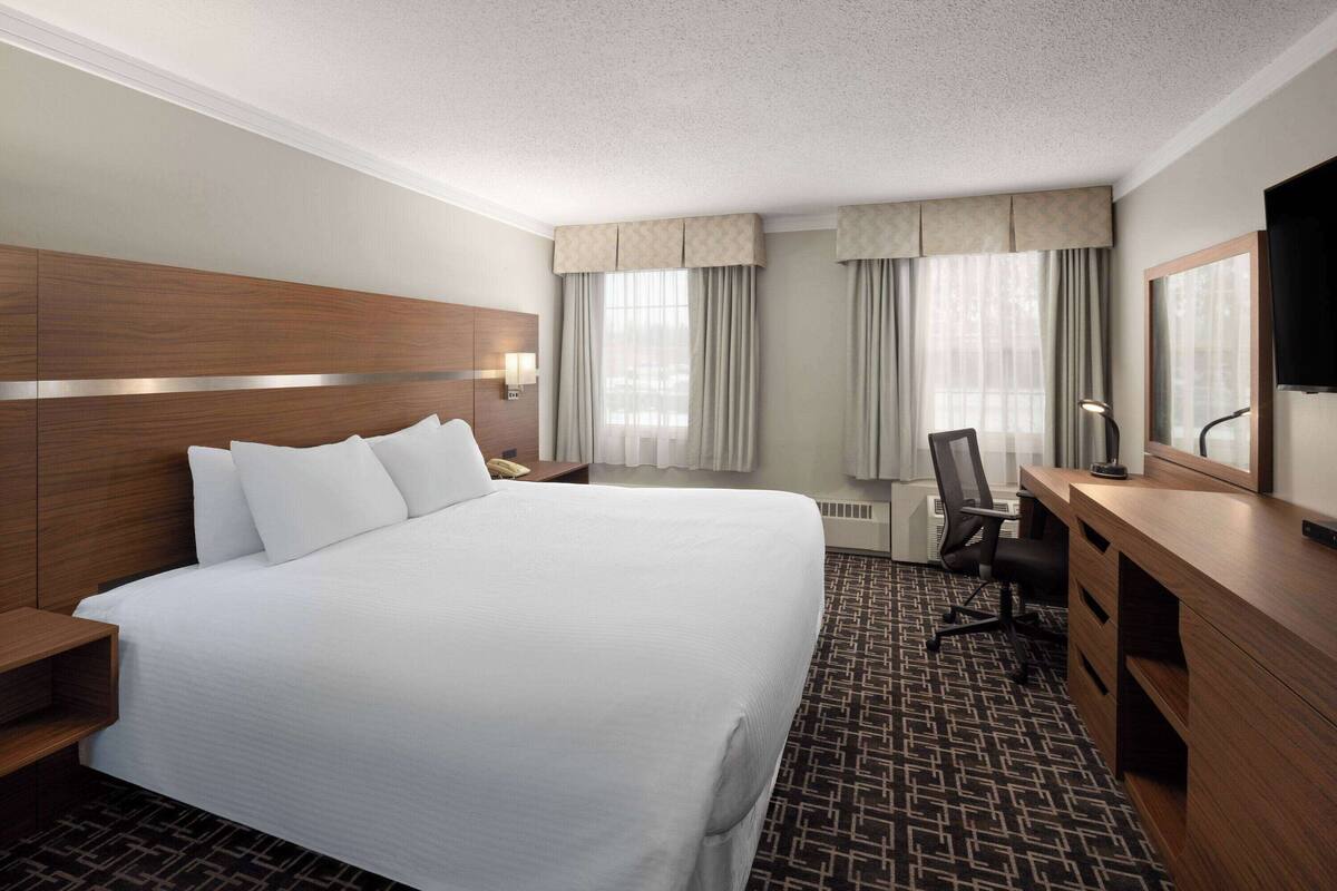 A hotel room with a large bed, a desk, a chair, a TV, and a window with curtains.