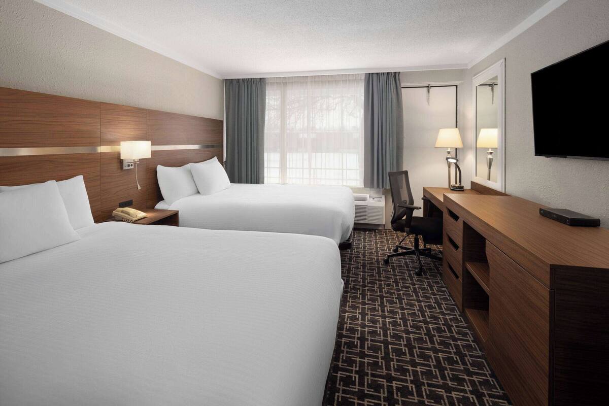 A hotel room with two beds, a desk, a chair, a TV, and a window with curtains.