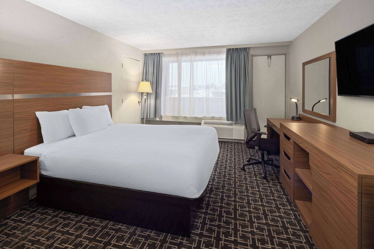 A hotel room with a large bed, a desk with a chair, a TV, and a window with curtains.