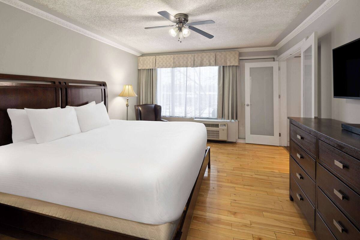 A hotel room with a large bed, a ceiling fan, a desk with a lamp, a TV, and a wardrobe.