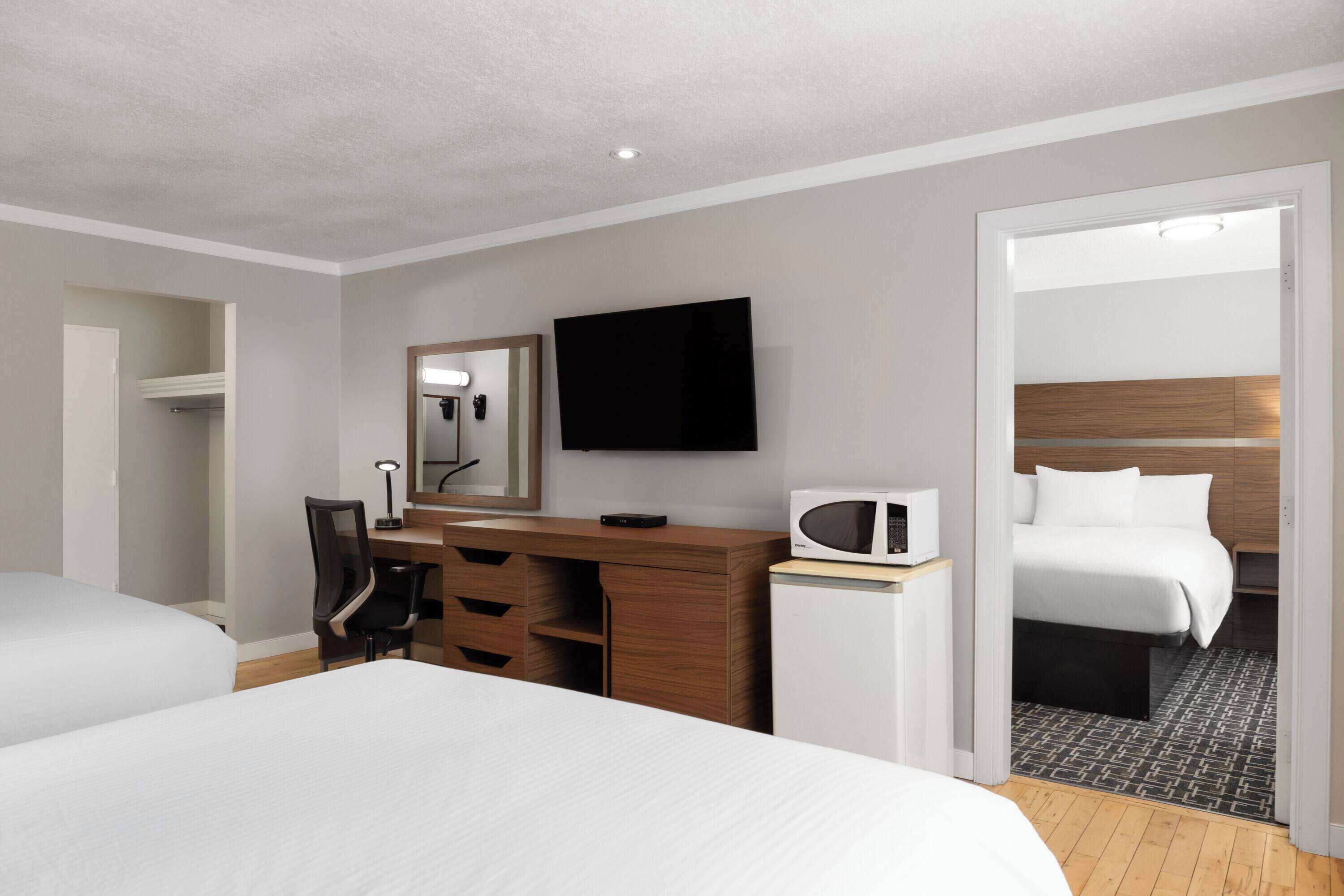 A hotel room with two beds, a desk with a chair, a flat-screen TV, a microwave, and a wardrobe.