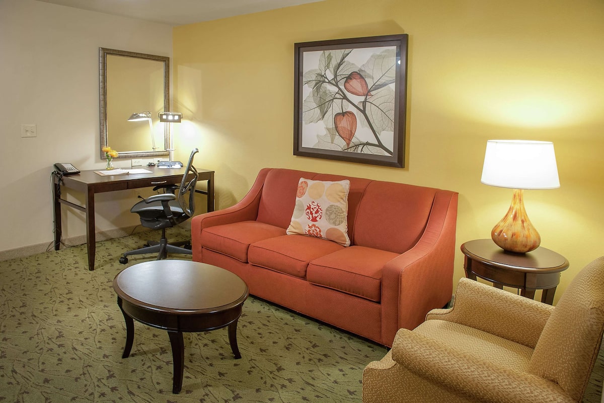 A living room with a sofa, a coffee table, a desk with a lamp, and a framed picture on the wall.
