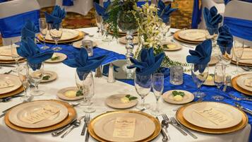 A table set for a formal event with blue napkins, gold-rimmed plates, and clear glassware.