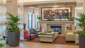 A spacious lobby with a high ceiling, multiple hanging pendant lights, a fireplace, comfortable seating, and large potted plants. - Hilton Garden Inn Pensacola Airport - Medical Center (Pensacola)