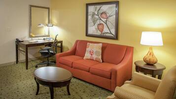 A furnished living room with a sofa, a coffee table, a desk with a lamp, a chair, and a painting on the wall.