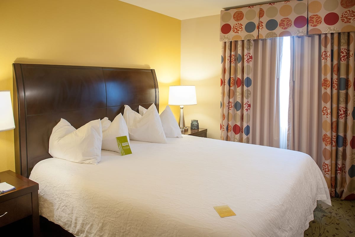 A hotel room with a large bed, a nightstand, a lamp, and a window with curtains.