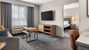 Habitación de hotel con cama, escritorio, silla, televisor y ventana con cortinas.