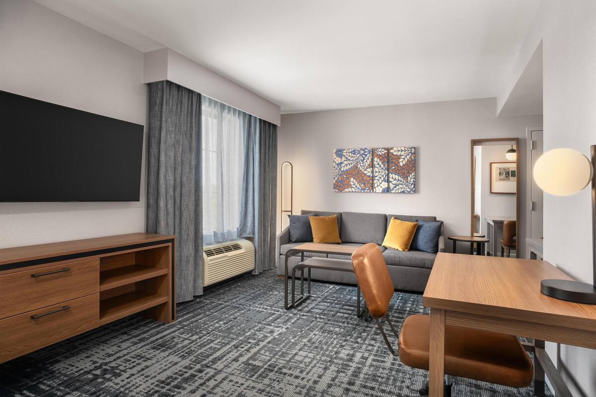 A hotel room with a desk, chair, sofa, and a large artwork on the wall.