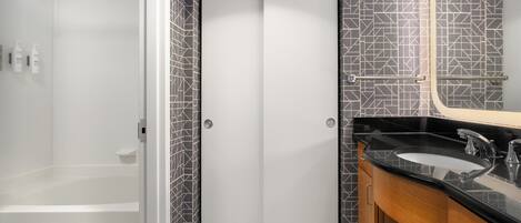 Une salle de bain avec une douche, une porte blanche, un lavabo avec un plan de travail noir et un miroir.
