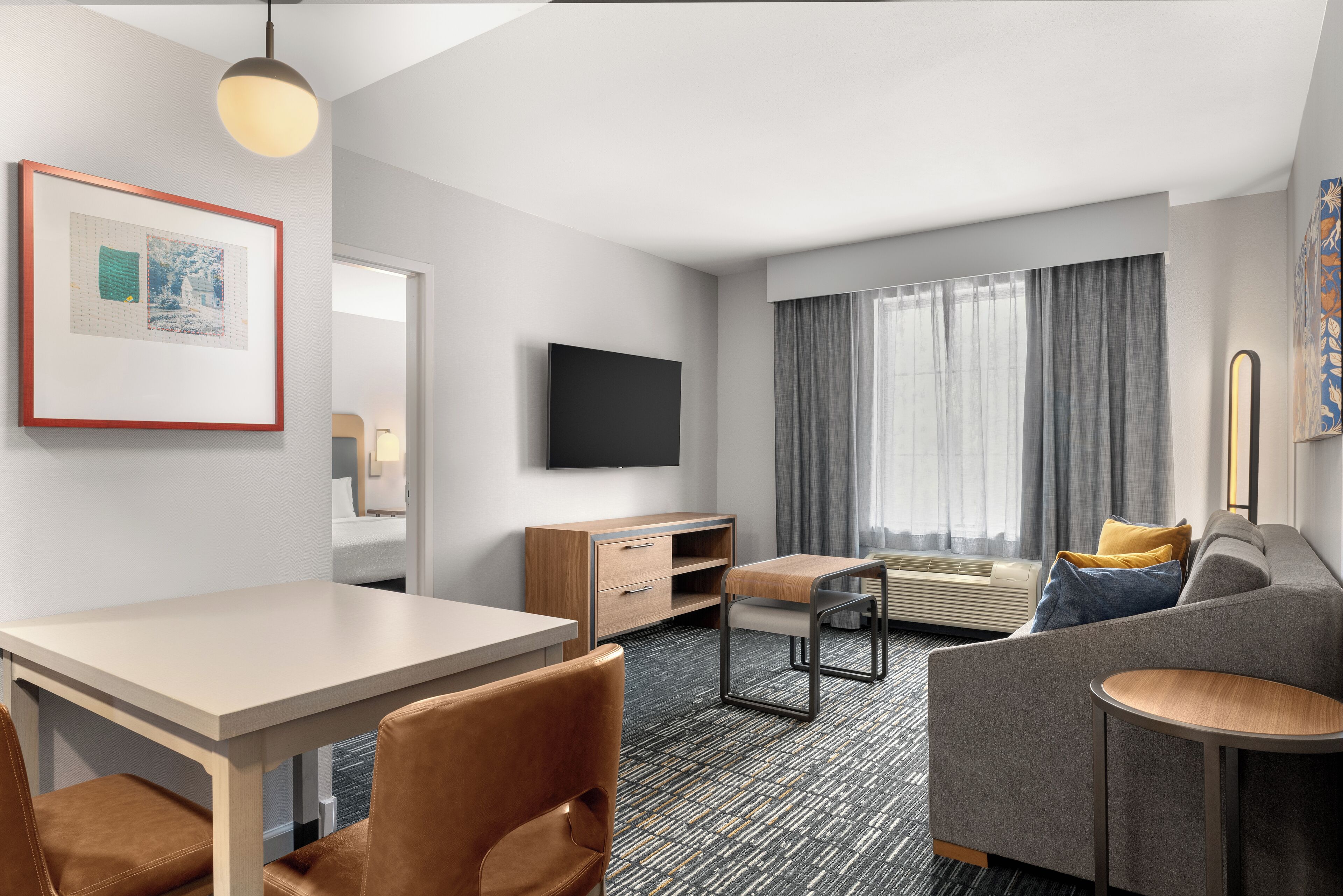 A modern hotel room with a flat-screen TV, a sofa, a dining table, and a desk.