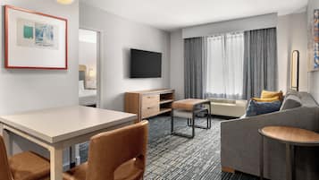 Quarto de hotel moderno com televisão de tela plana, sofá, mesa de jantar e escrivaninha.