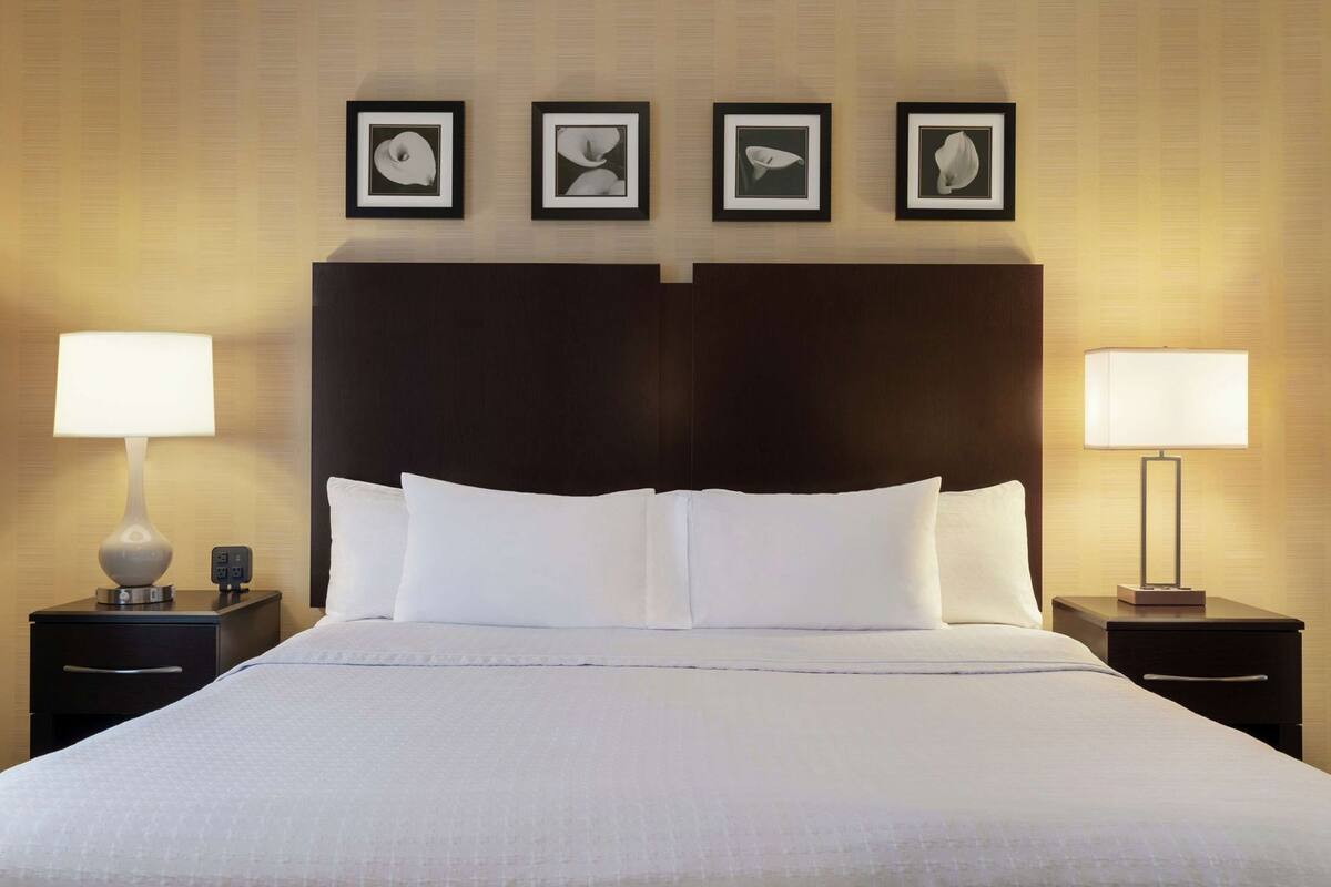 A hotel room with a large bed, two bedside tables with lamps, and four framed pictures on the wall.